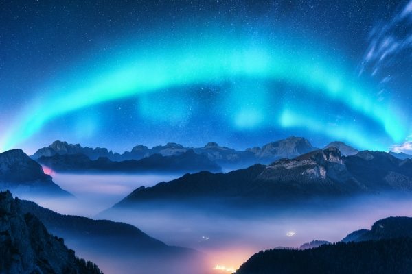 Aurora borealis above mountains in fog at night